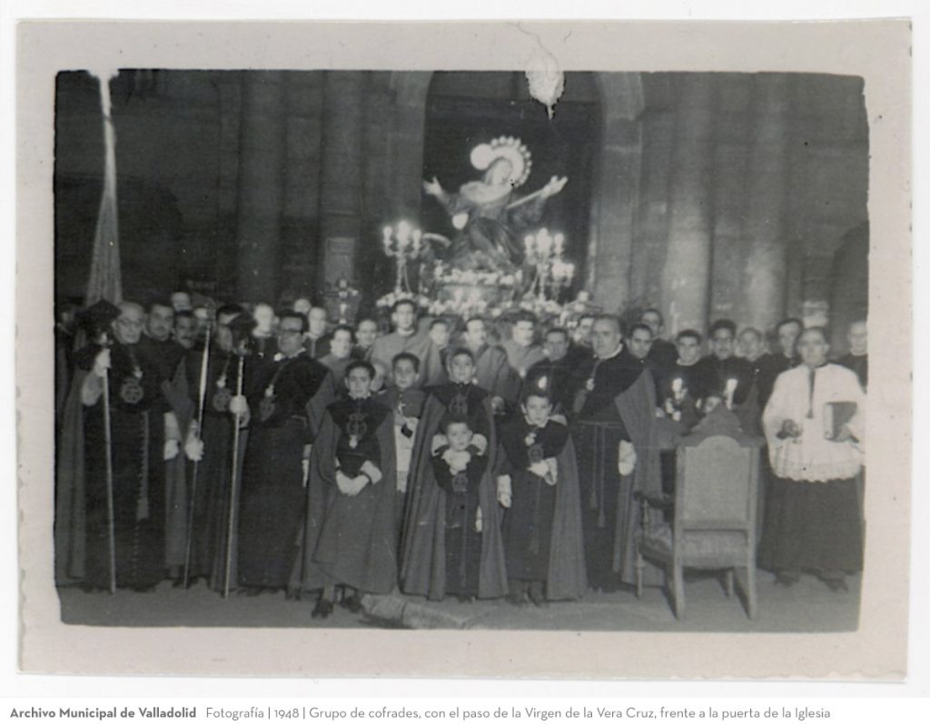 Fotografía. 1948. Grupo de cofrades, con el paso de la Virgen de la Vera Cruz, frente a la puerta de la Iglesia